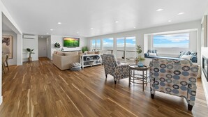 A spacious living room with hardwood flooring, a large sofa, a patterned armchair, and a television on the wall. - Hot tub on the Beach with Super-Fast Wi-Fi (Oak Harbor)