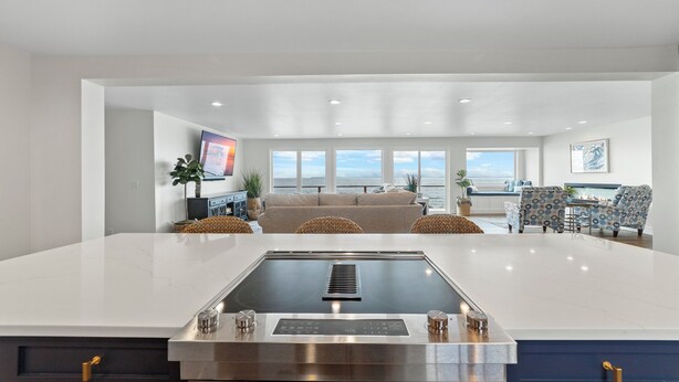 A modern kitchen with a central island, a dining area with patterned chairs, and a view of the ocean. - Hot tub on the Beach with Super-Fast Wi-Fi (Oak Harbor)