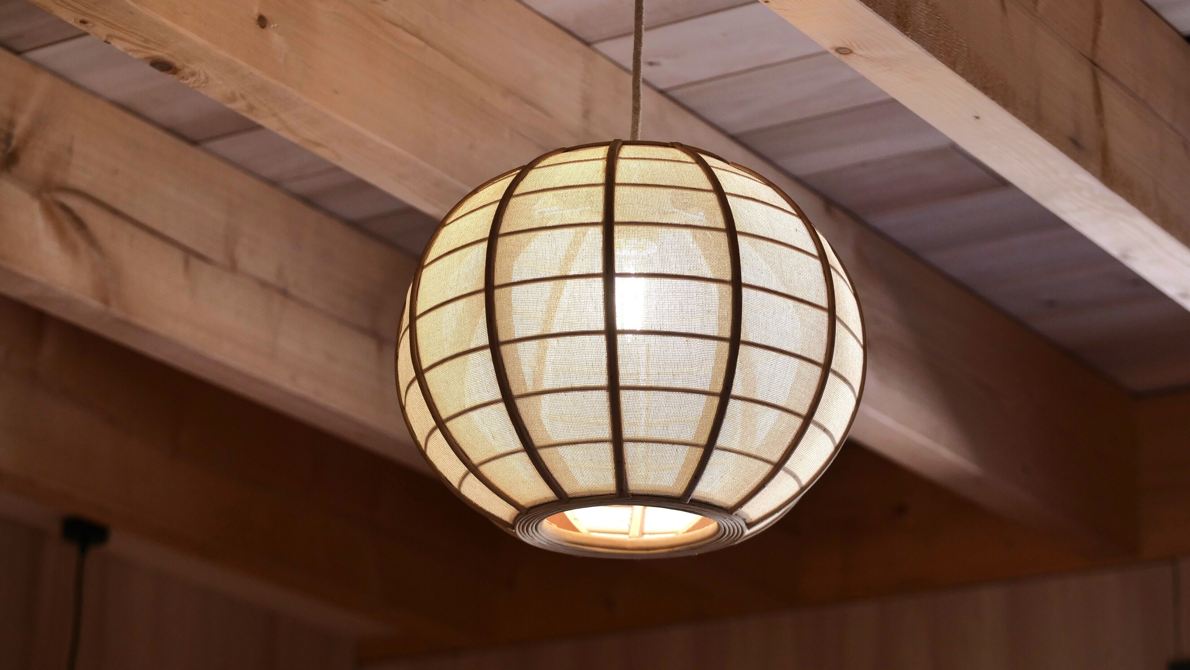 A hanging spherical lantern with a grid pattern, suspended from a wooden ceiling.