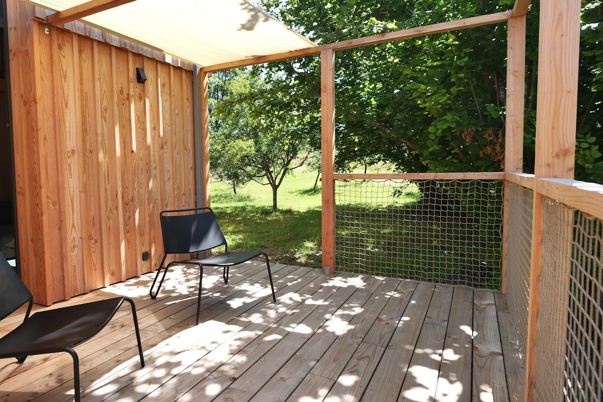 A wooden deck with two black chairs, a wooden wall, and a view of a grassy area with trees.
