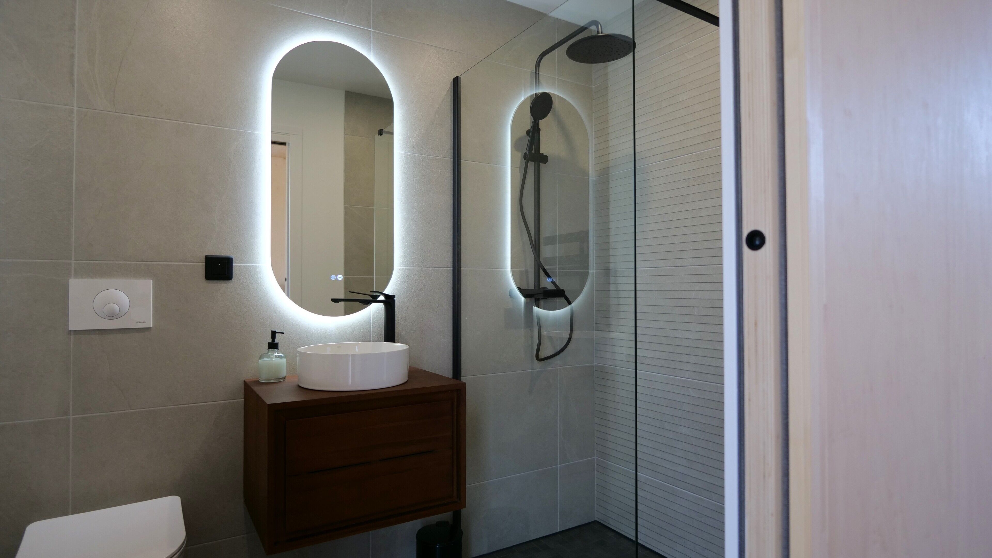 A modern bathroom with a round mirror, a sink, and a shower.