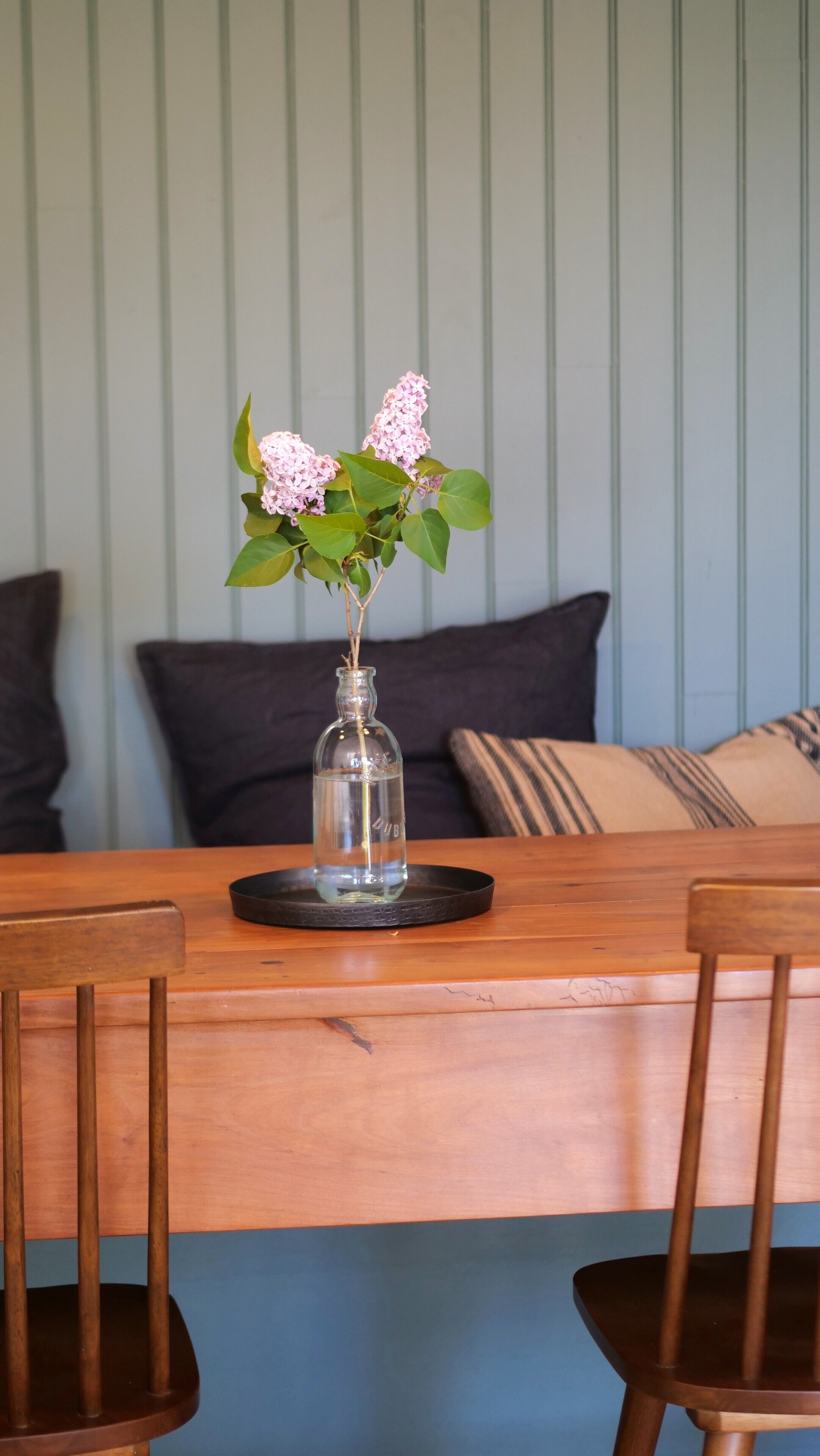 A dining table with a clear glass vase containing pink flowers, set against a striped wall.