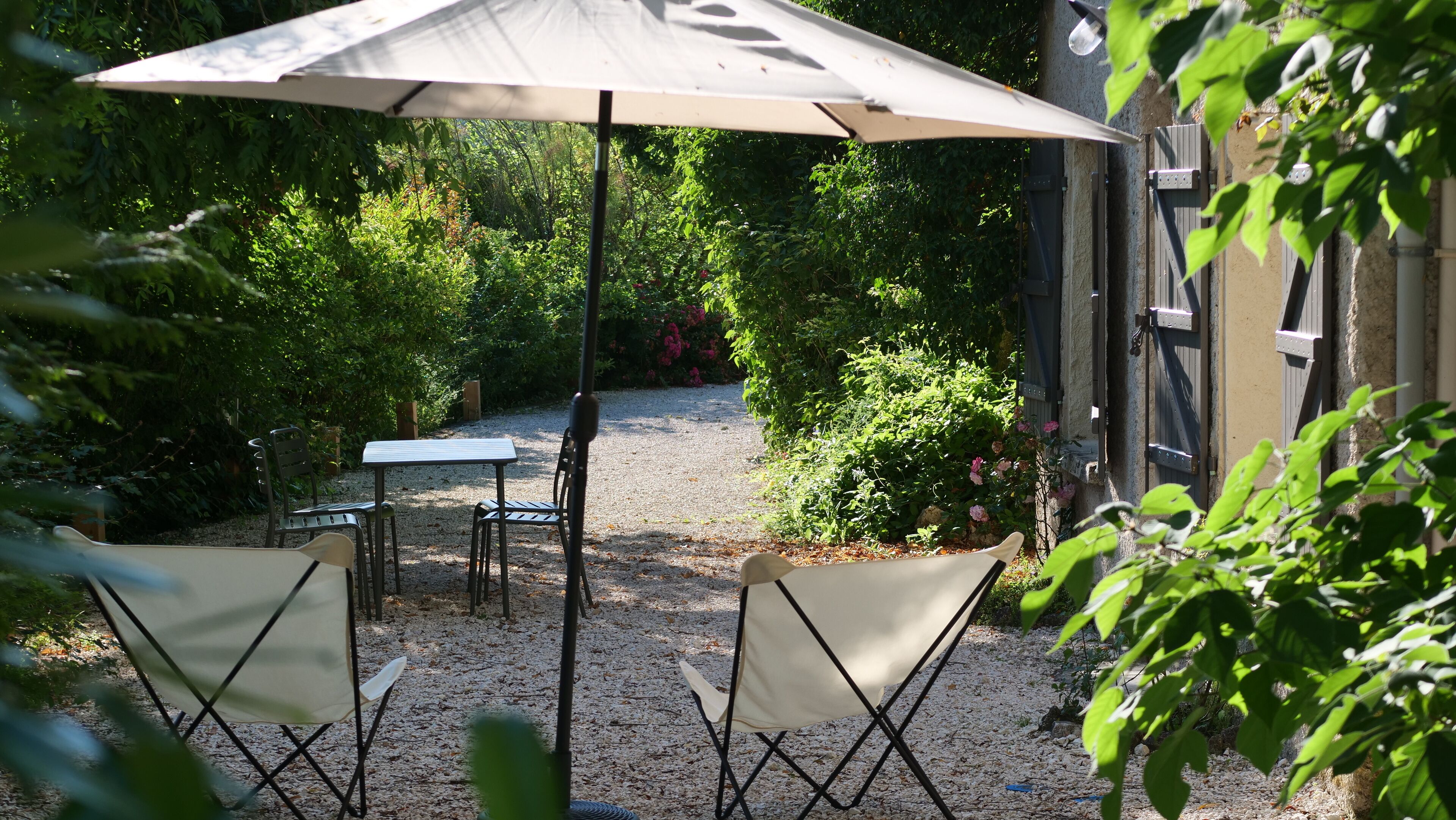 An outdoor patio with a table and two chairs, surrounded by gravel and greenery.
