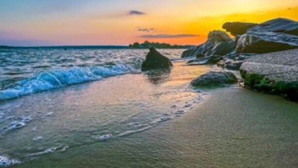 Una playa con olas y rocas al atardecer.