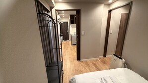 Hotellihuoneessa on sänky, puulattia, musta metallihylly ja näkymä keittiötilaan.