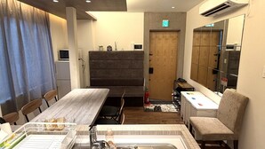 Hotellihuone, jossa on puinen ruokapöytä, pieni keittokomero, pesuallas, peili ja penkki.