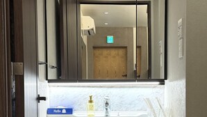 Moderni kylpyhuone, jossa on suuri peili, valkoinen pesuallas ja tummat puukaapit.