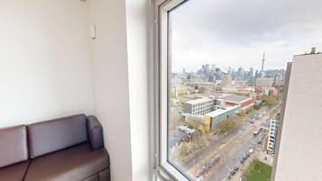 A room with a large window, a brown sofa, and a view of a cityscape with buildings and a tower.