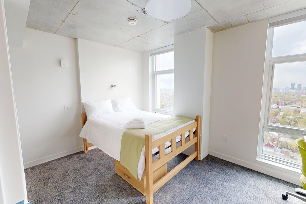 Ein Schlafzimmer mit Bett, Fenster, Sessel und Blick auf die Stadt.