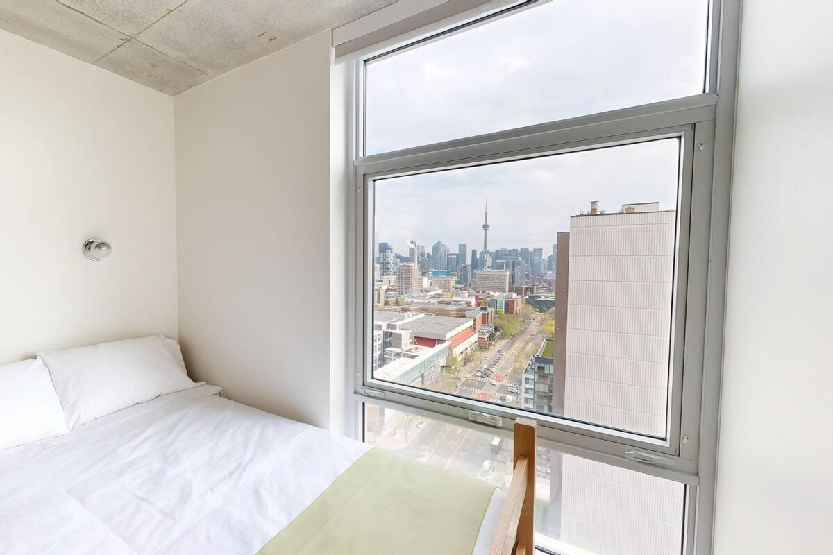 Ein Schlafzimmer mit großem Fenster, einem Bett und Blick auf eine Stadtlandschaft.