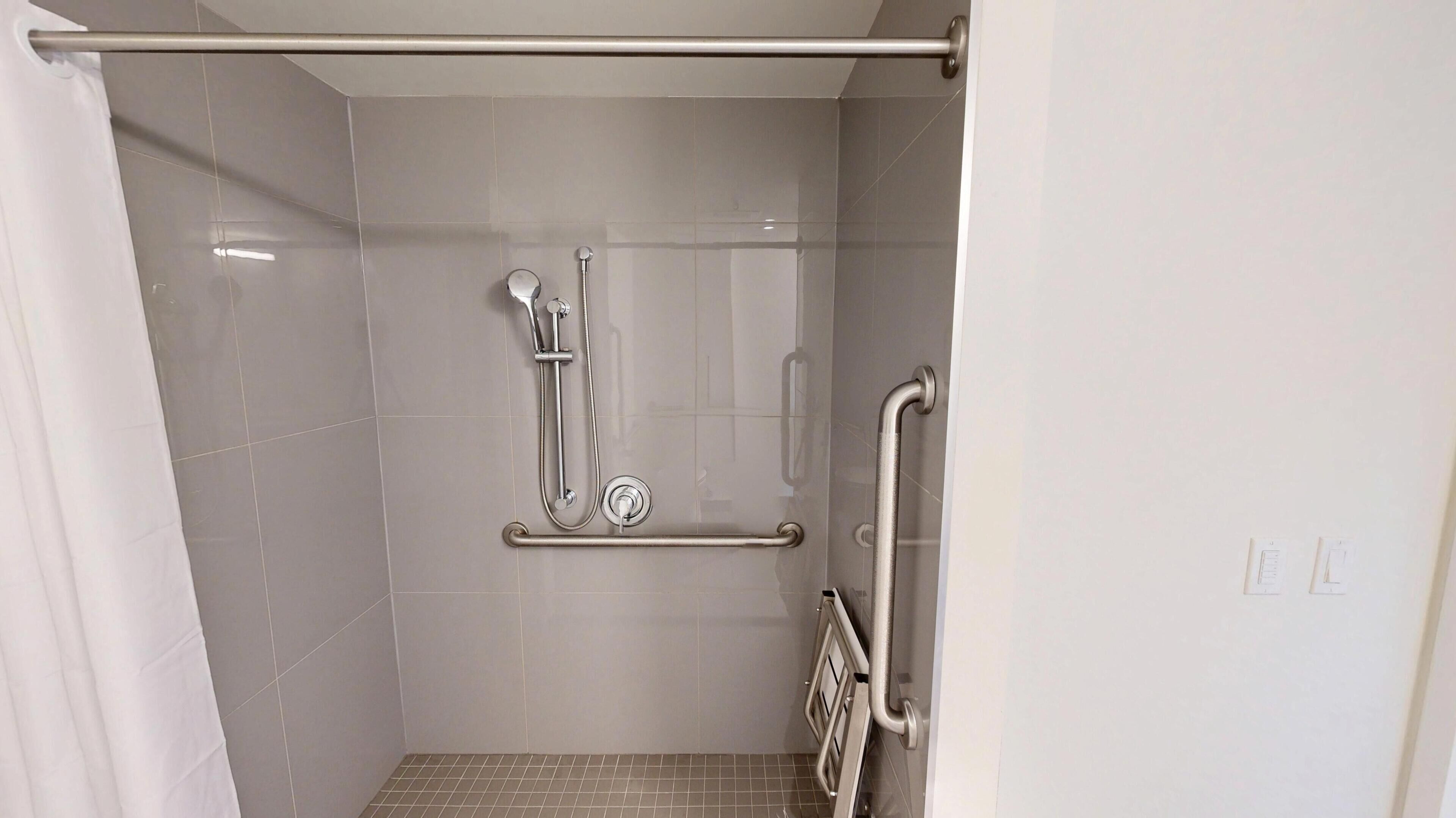 A shower with a grab bar, a handheld showerhead, and a floor-mounted control.