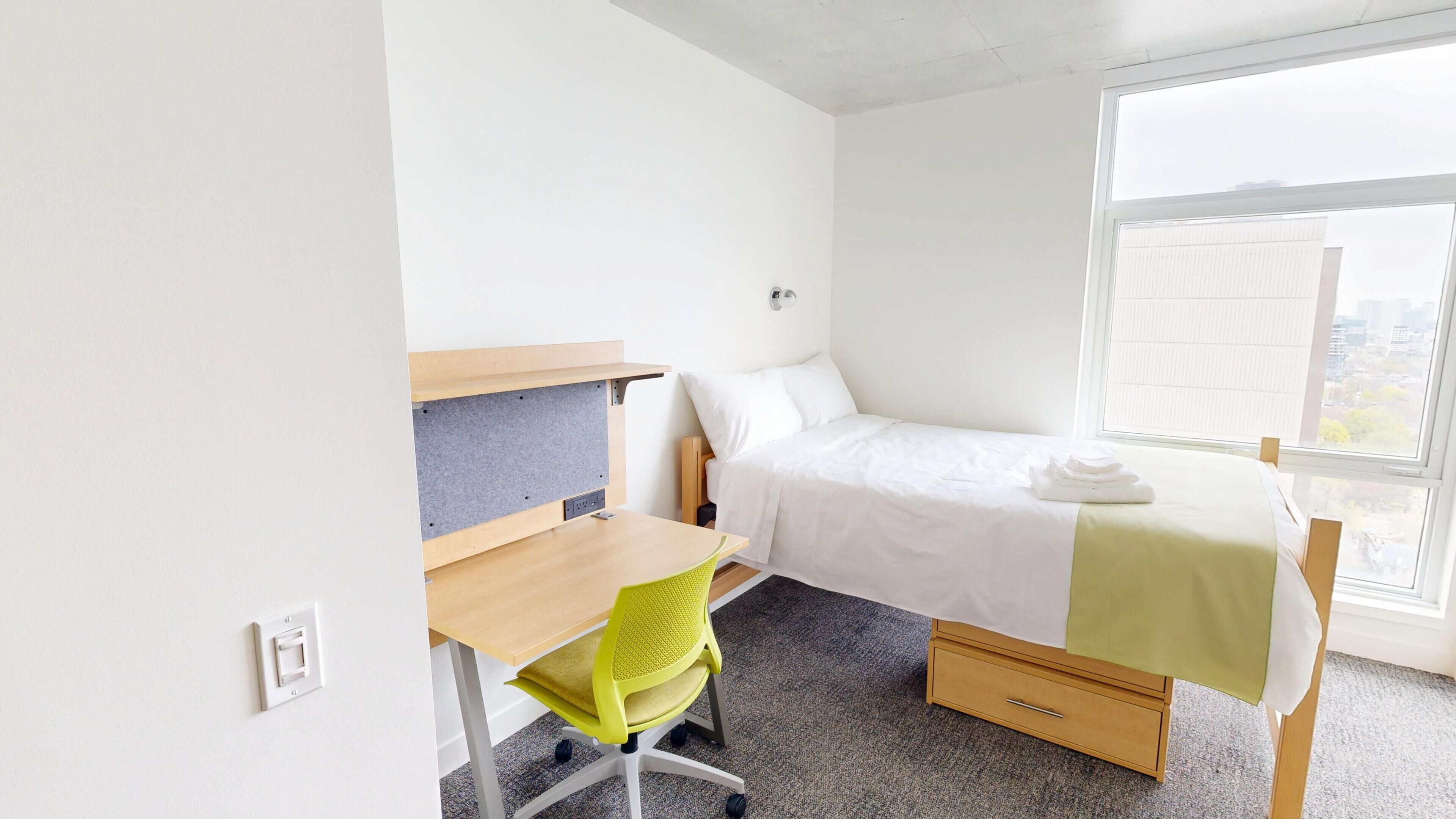 Een kleine, schone kamer met een bed, een bureau en een stoel.