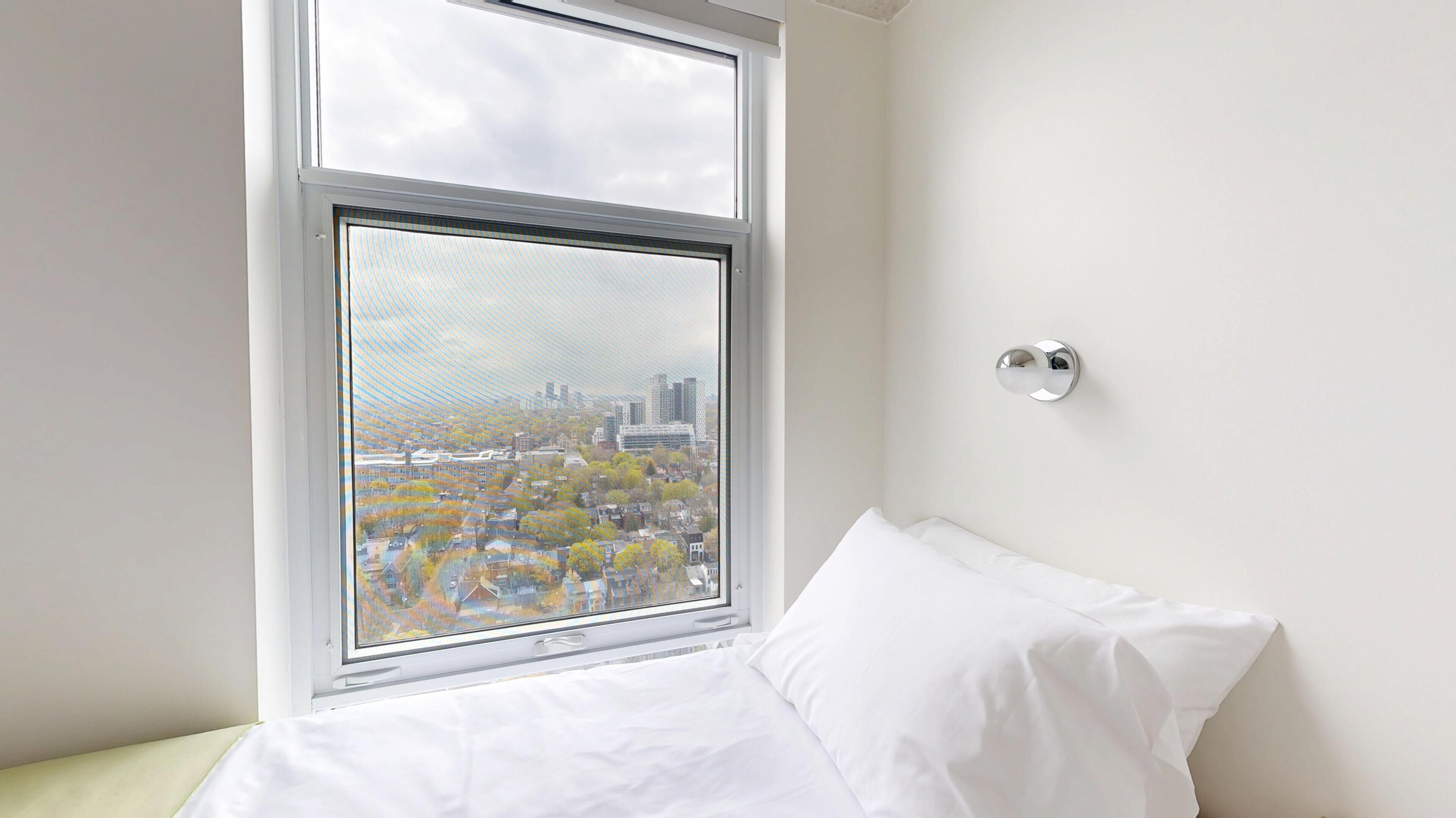 A bedroom with a large window, a bed, and a wall-mounted light fixture.