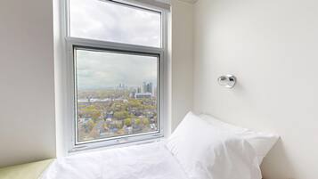 A bedroom with a large window, a bed, and a wall-mounted light fixture.
