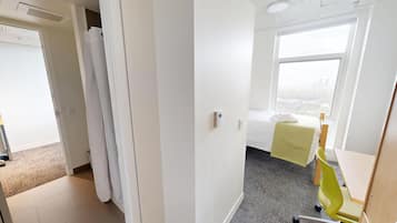 Une chambre d’hôtel comprenant un lit, une fenêtre donnant sur la ville, un bureau avec une chaise et une porte menant à une autre pièce.