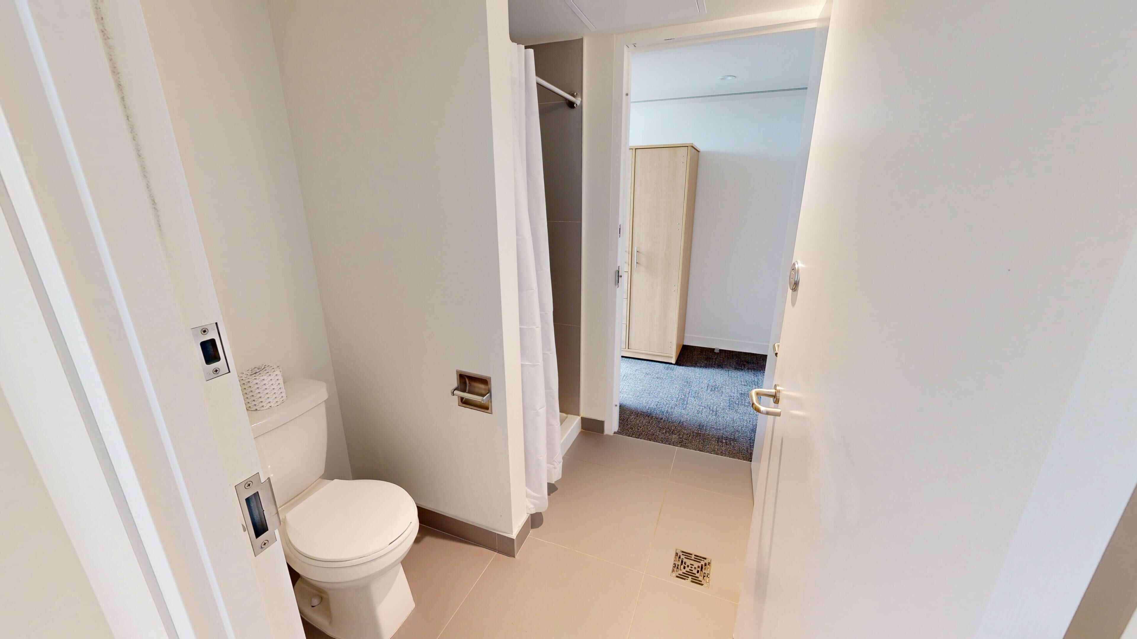 A small, clean bathroom with a toilet, a shower curtain, and a door leading to another room.