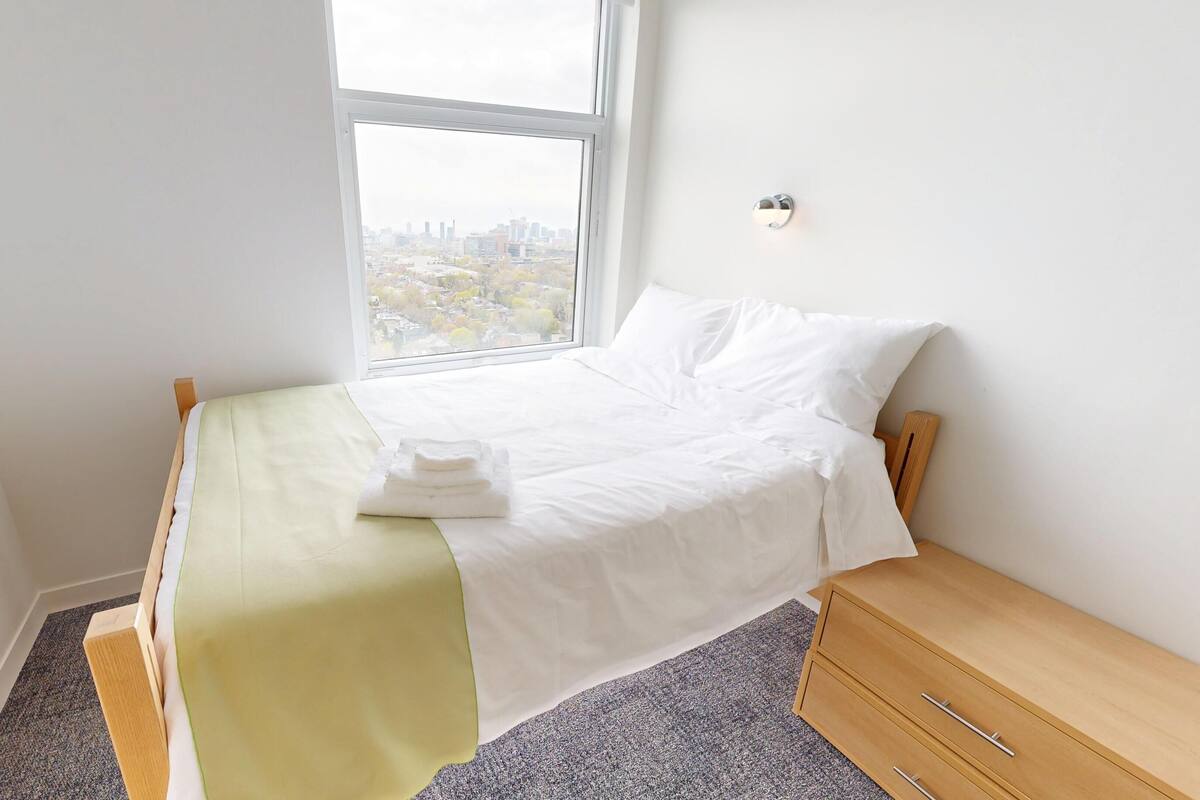 Ein Einzelbett mit weißer Bettwäsche, einer grünen Tagesdecke und einem Nachttisch mit Schubladen.