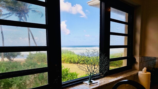 Uma casa de banho com vista para a praia através de uma janela.