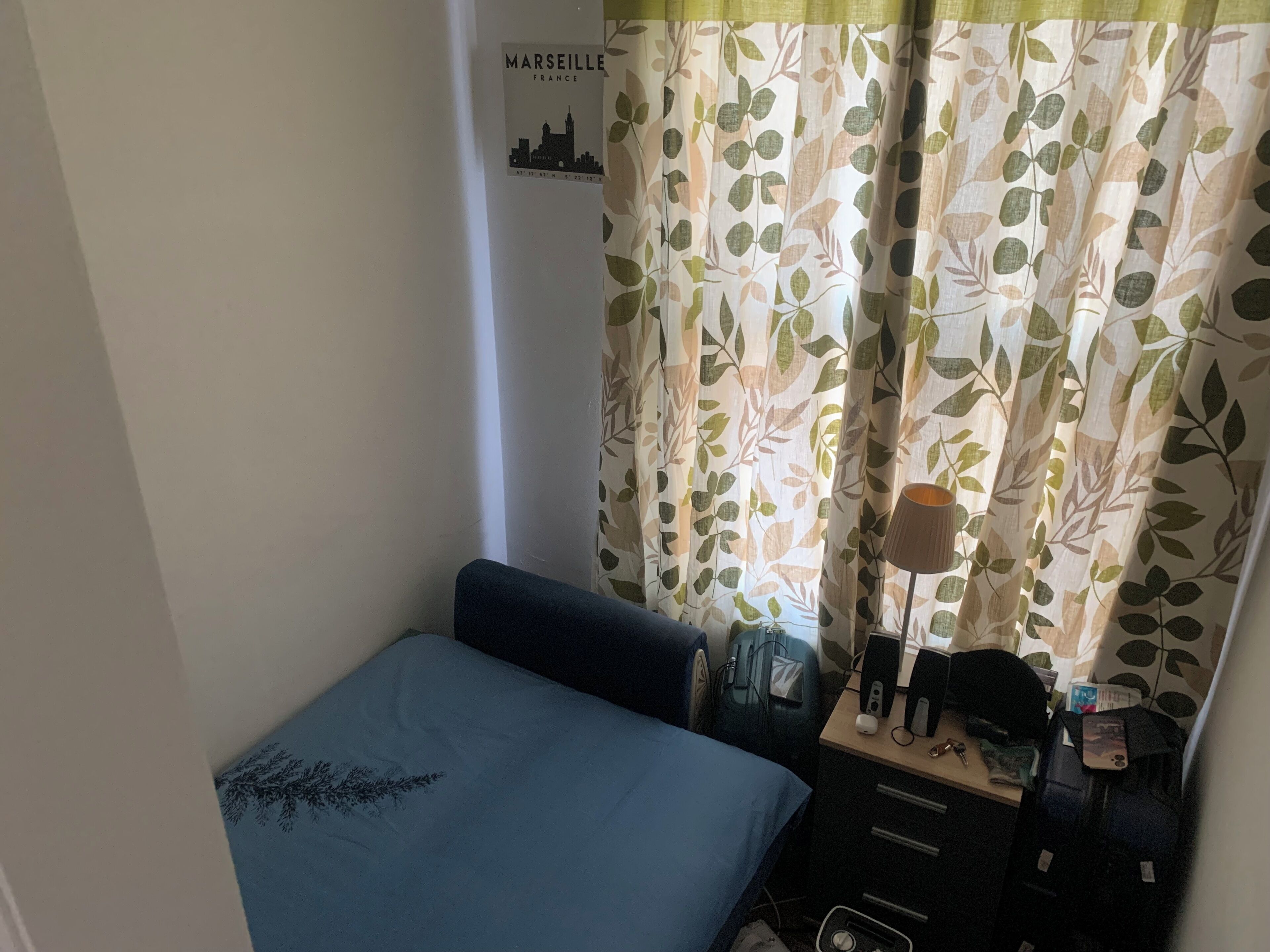 Una habitación pequeña con una cama, un escritorio con una lámpara y una cortina con estampado de hojas.