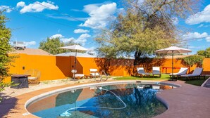 A swimming pool with lounge chairs and umbrellas, surrounded by orange walls and trees. - Stylish 6BR Home, Pool, Sleeps 12,Near Old Town (Scottsdale)