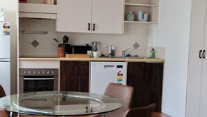 Een moderne keuken met een ronde glazen tafel en vier bruine stoelen, een inbouwoven en een vaatwasser.