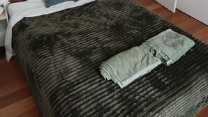 Een slaapkamer met een bed, kussens, een deken en een handdoek.
