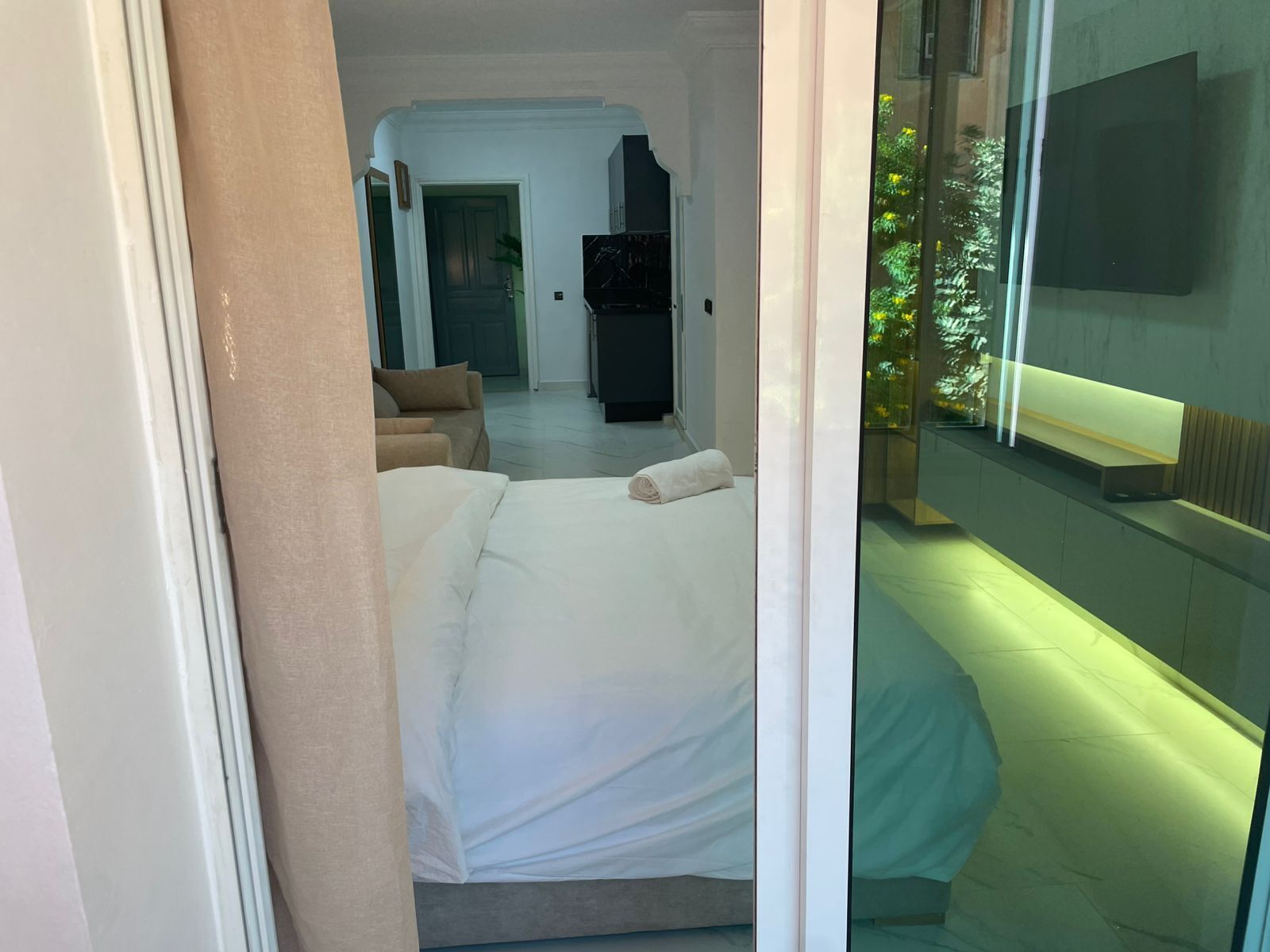 Ein Hotelzimmer mit Bett, Sofa, Fernseher und einer Glaswand mit Blick auf Grünflächen.