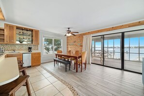 A modern kitchen with wooden cabinets, a dining table, and a view of the water. - The Flip Side | Private Dock w/ Tie Up | Little Lagoon | My Beach Getaways (Gulf Shores)