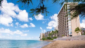 Een strandhotel met meerdere balkons, een zandstrand en palmbomen.
