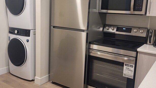 A compact kitchen with a stainless steel refrigerator, a microwave, and an oven. - Beautiful new basement homeclose to greenery (Saskatoon)
