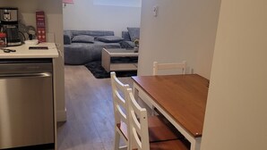 A compact kitchen with a coffee maker, a small refrigerator, and a dining area with a wooden table and white chairs. - Beautiful new basement homeclose to greenery (Saskatoon)
