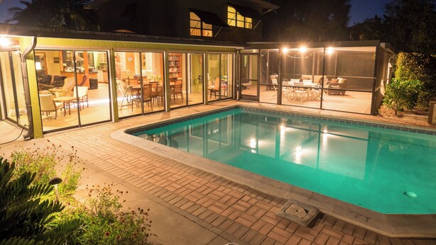 A modern house with a swimming pool, glass doors leading to a patio with outdoor furniture, and a well-lit interior. - Private Home on Canal w/ Heated Pool, Walk to Siesta Key Beach & Village (Siesta Key)