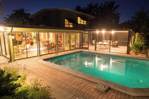 A modern house with a swimming pool, glass doors leading to a patio with outdoor furniture, and a well-lit interior. - Private Home on Canal w/ Heated Pool, Walk to Siesta Key Beach & Village (Siesta Key)