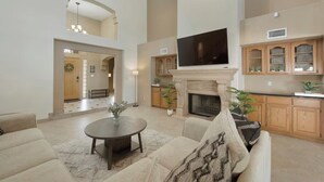 A spacious living room with a fireplace, a television mounted above it, and a kitchen area with wooden cabinets.