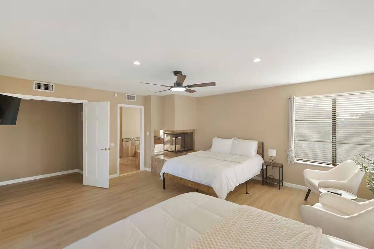 A bedroom with a bed, a chair, a nightstand, a ceiling fan, and a window with blinds.