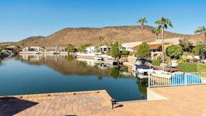 A marina with boats docked, a clear blue sky, and a hilly landscape in the background.