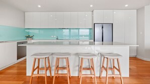 A modern kitchen with a large island, white cabinetry, and wooden stools.