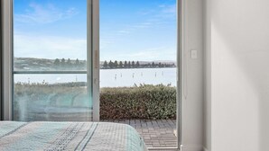 A bedroom with a large sliding glass door leading to a balcony with a view of a lake and distant trees.