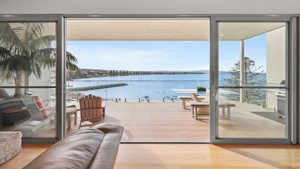 A modern living room with a large sliding glass door leading to a balcony overlooking a body of water.