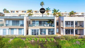 A modern multi-story hotel with a prominent "HARRIS" sign, featuring balconies, large windows, and a landscaped front garden.