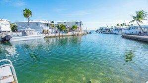 A marina with boats docked, a white house with a balcony, and palm trees. - Canalfront Coastal Retreat w/Open Water Views & Fishing Dock (Cudjoe Key)