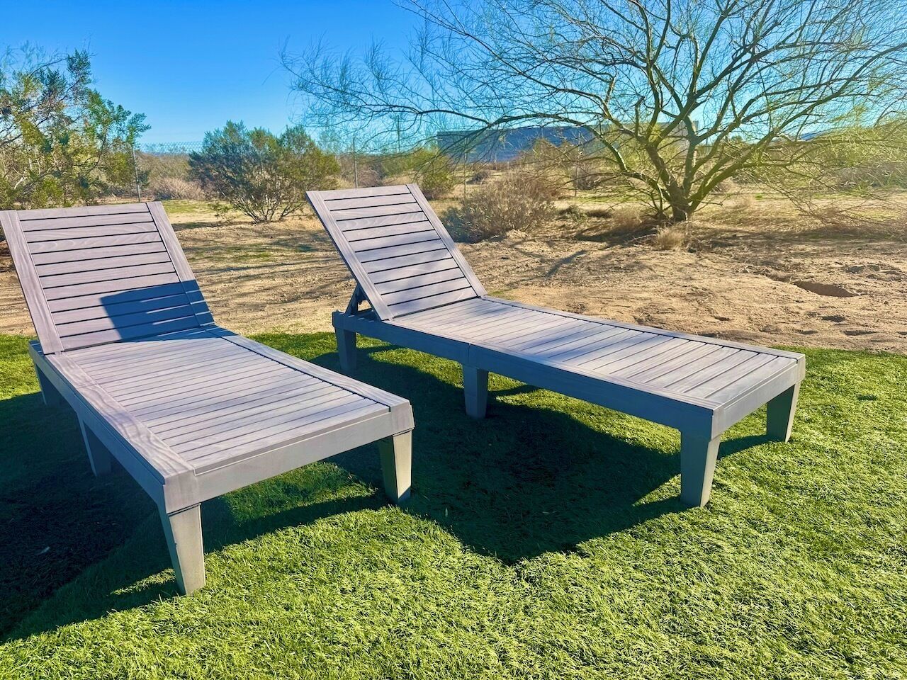 Deux fauteuils de jardin en bois, placés sur une pelouse bien entretenue, offrent une vue dégagée sur un paysage naturel en arrière-plan.