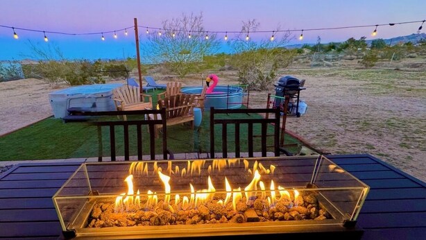 A deck with a fire feature, outdoor furniture, and string lights against a desert backdrop. - Desert Game House with Hot Tub and Stargazing (Joshua Tree)