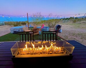 Una terraza con una chimenea, muebles de exterior e iluminación de luces colgantes, con el paisaje desértico de fondo.