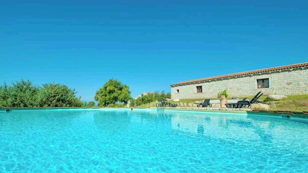 A clear blue pool with lounge chairs and a stone building in the background. - Holiday Apartment La Pietraia Two-Room Apartment (Badesi)