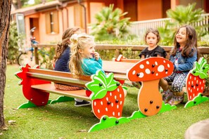 Children sitting on a bench with a unique design featuring large mushroom shapes. - Holiday apartment Two-room apartment with air conditioning (Albinia)