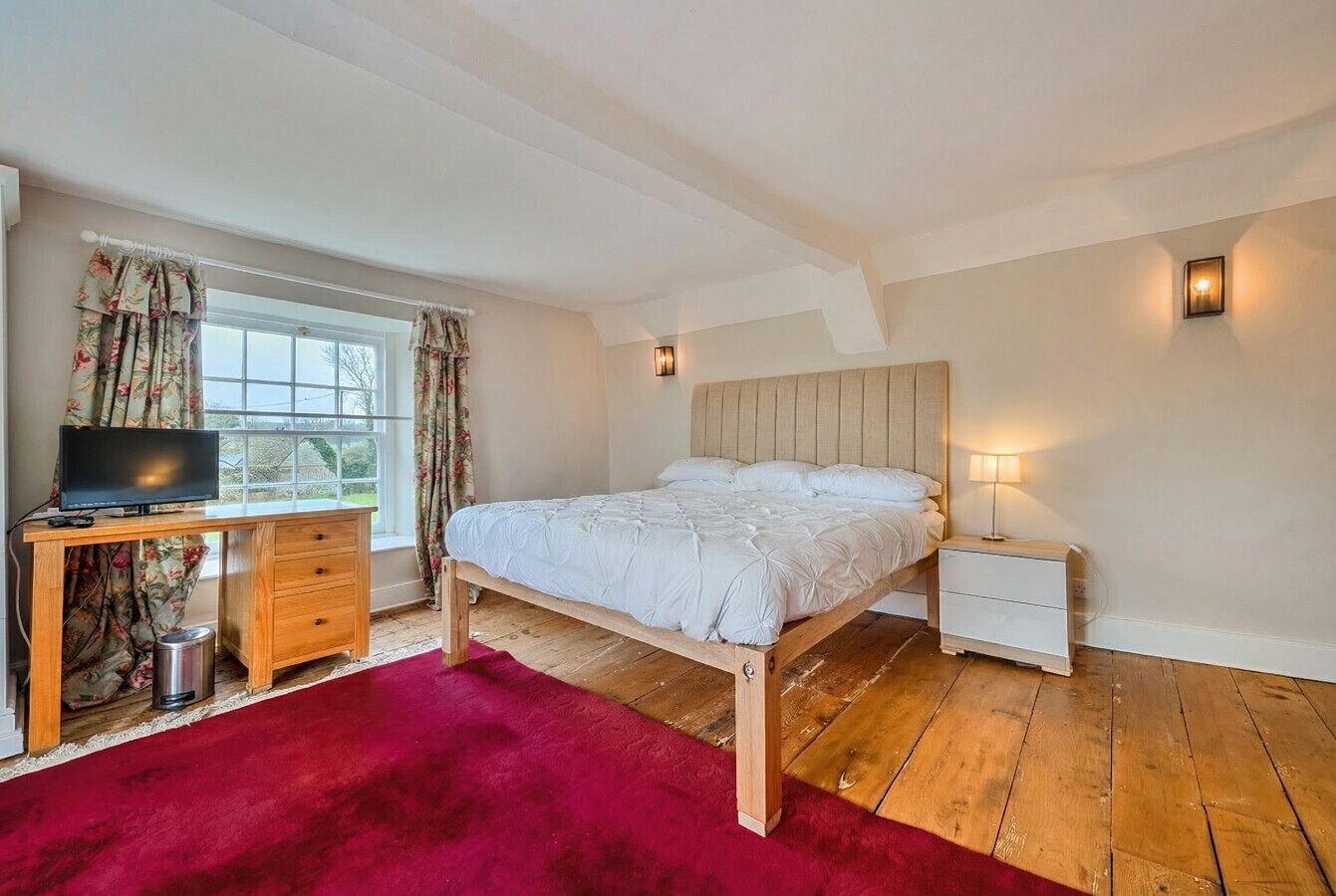 Een slaapkamer met een bed, een bureau, een televisie, een nachtkastje en een raam met gordijnen.