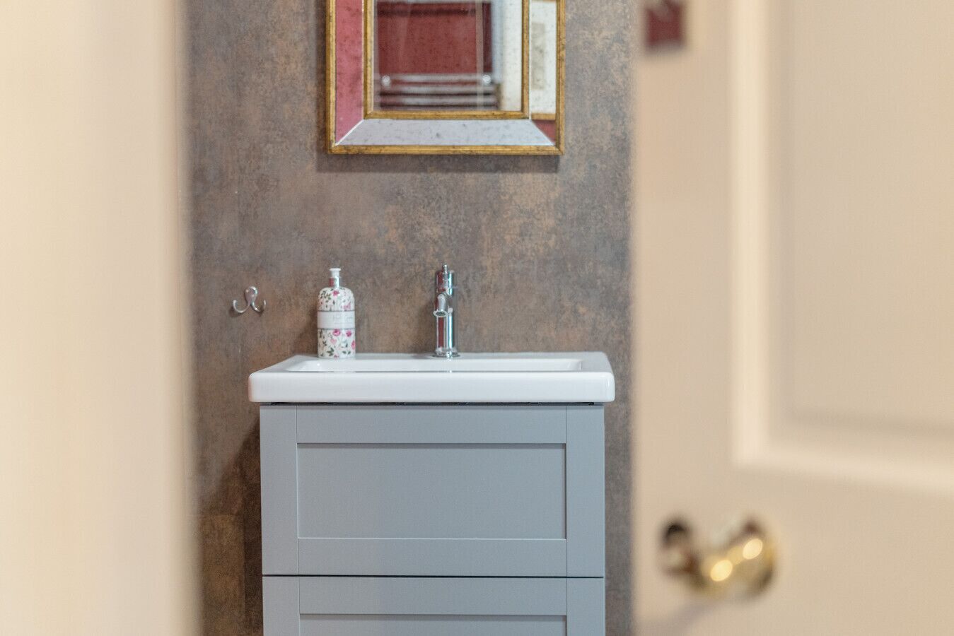 A bathroom with a white sink, a mirror, and a bottle of soap.
