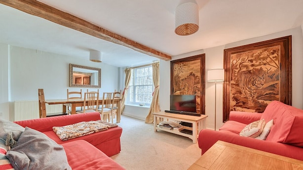 A living room with red sofas, a wooden coffee table, a TV on a stand, a dining table with chairs, and artwork on the walls.