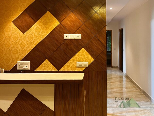 A modern hotel interior with a geometric patterned wall, a reception desk, and a hallway leading to a door. - The Croft Bnb (Shimla)